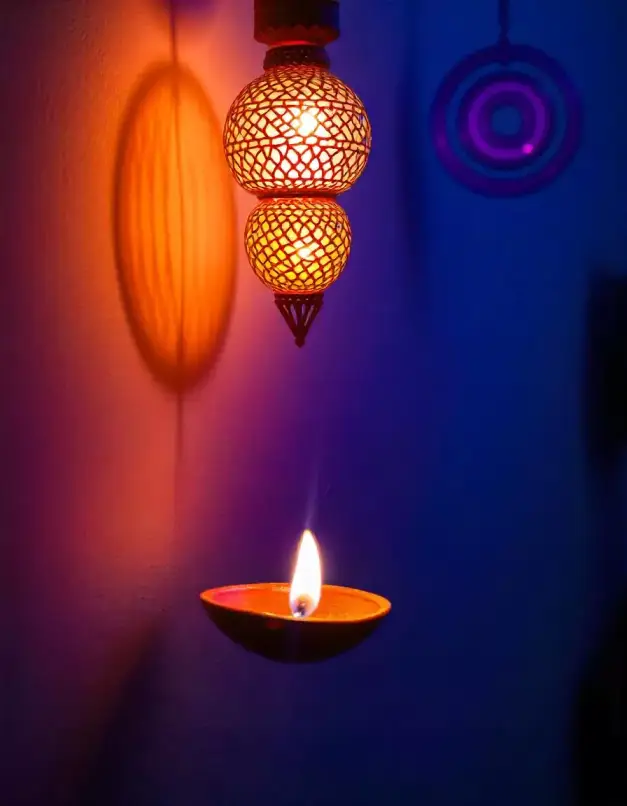 A hanging decorative lantern with a diya flame casting warm and colorful shadows on a wall, creating a festive ambiance. | Decorative Hanging Lantern with Diya for Festival Lighting | Festival Indoor Decoration Ideas | Decorations Guru