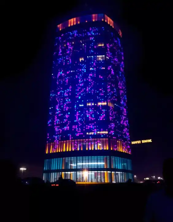 A tall cylindrical building illuminated with purple, blue, and orange lights during Diwali night celebration | Festival Tower Light Decoration | Festival Outdoor Decorations | Decorations Guru